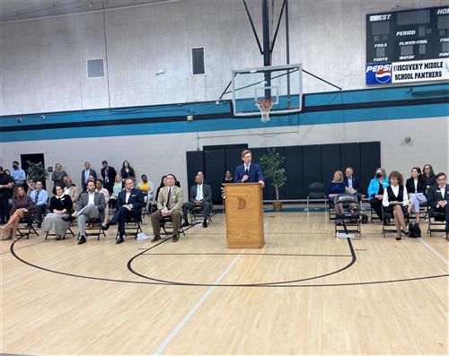 Wide angle photo of dignitaries seated in gym for Milken presentation Discovery Middle